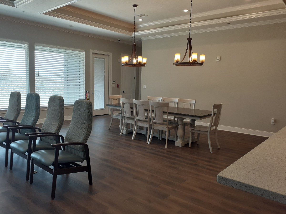 A modern dining room with a large table, elegant chandeliers, and hardwood flooring.