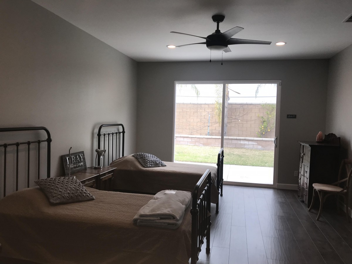 A minimalist bedroom with twin beds and large windows overlooking a backyard.