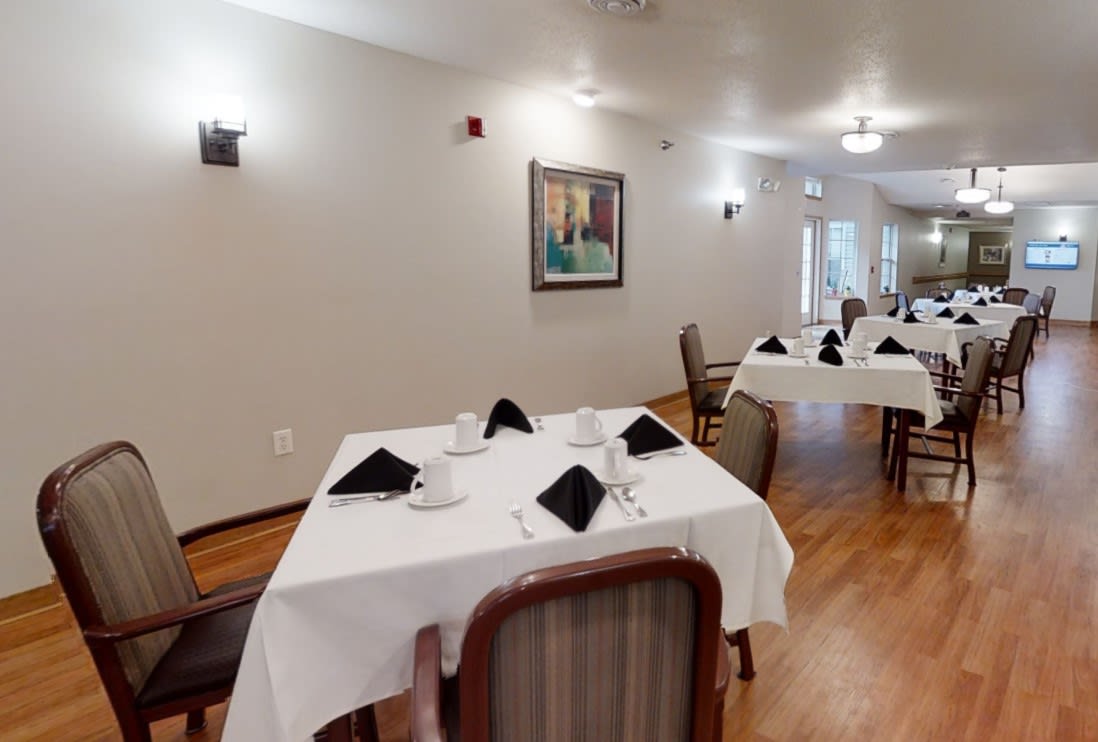 A cozy dining area with neatly arranged tables and chairs, featuring elegant table settings and a wall painting.