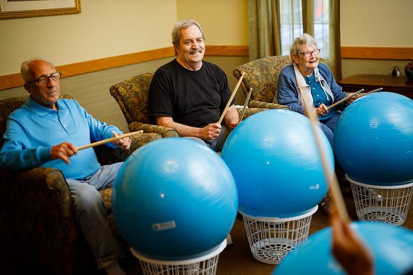 Seniors participating in a group exercise session using therapy balls and drum sticks.