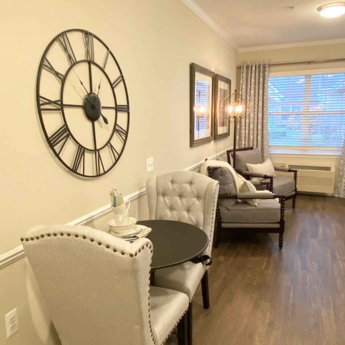 A cozy living room with elegant furniture, featuring a large wall clock and framed artwork.