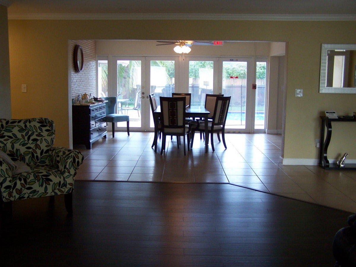 A view of a dining room with a table and chairs, large windows, and tiled flooring.