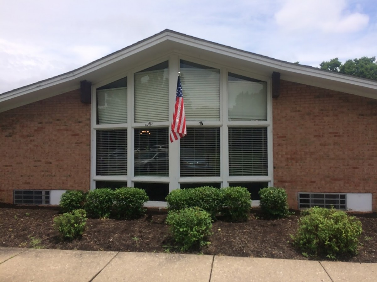 A brick building with large windows and an American flag displayed above neatly trimmed bushes.