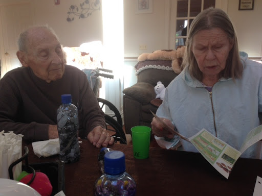 Two elderly individuals engaged in conversation at a table, surrounded by food and drinks.