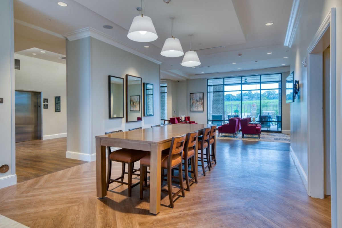 A spacious and modern dining area with a wooden table, surrounded by chairs and illuminated by pendant lights, featuring large windows for natural light.
