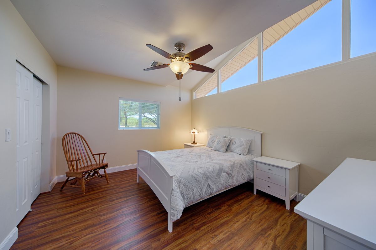 A cozy bedroom with a white bed, wooden flooring, and a ceiling fan.