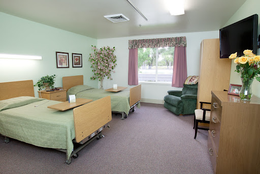 A well-lit hospital room with two beds, a window with curtains, and comfortable furniture.