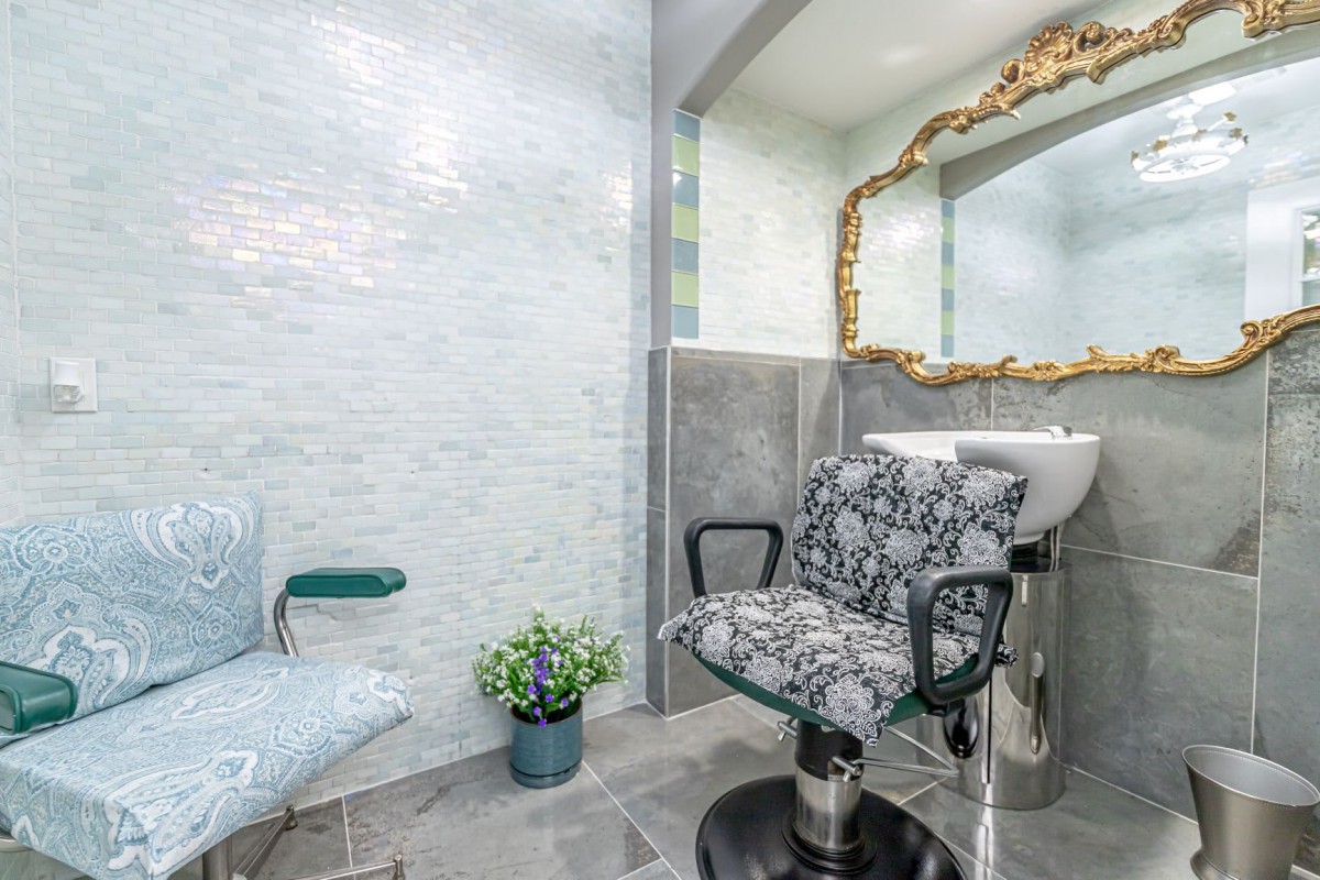 A stylish salon interior featuring a patterned chair, ornate mirror, and modern sink.