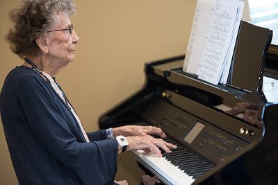 An elderly person playing the piano with sheet music in front of them.