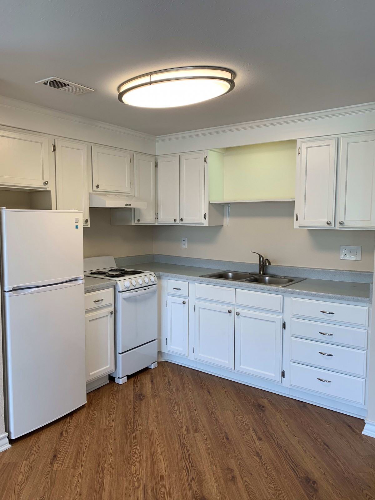 A modern kitchen with white cabinets, featuring a refrigerator, stovetop, and sink.