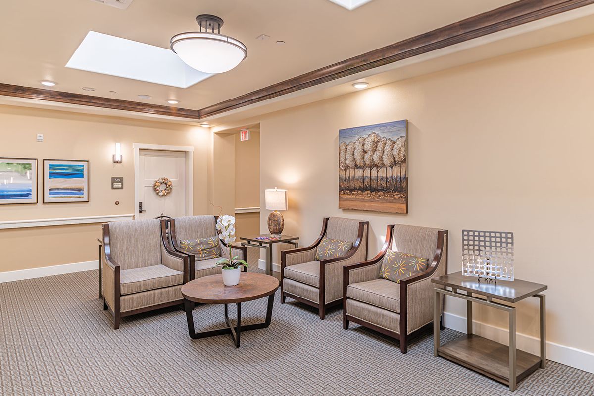 A well-lit waiting room featuring comfortable chairs, a central table, and artwork on the walls.