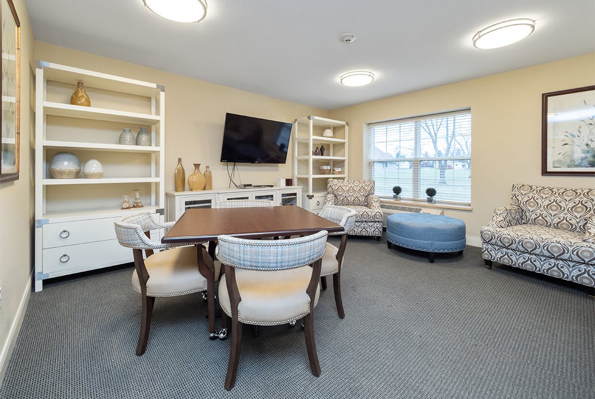 A modern living room with a dining table, chairs, and a television mounted on the wall.