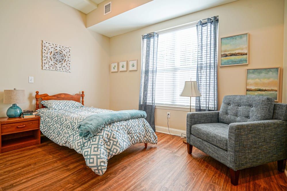 A cozy bedroom with a single bed, armchair, and natural light coming through the window.