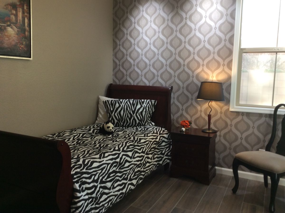A cozy bedroom featuring a single bed with zebra print bedding, a nightstand with a lamp, and decorative wallpaper.