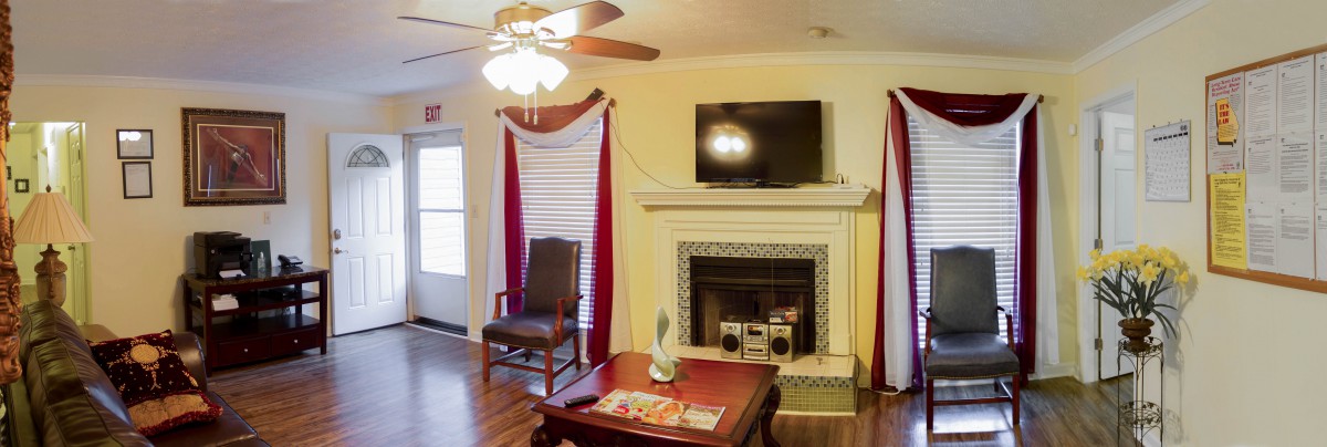 A cozy living room with a fireplace and a television mounted above it, complete with red curtains and a ceiling fan.