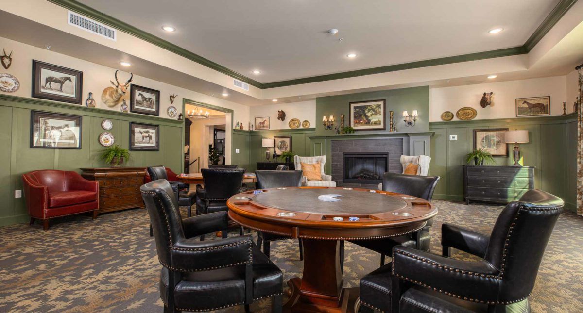 A luxurious poker room featuring a round gaming table surrounded by leather chairs, set within a cozy ambiance highlighted by green walls and a fireplace.