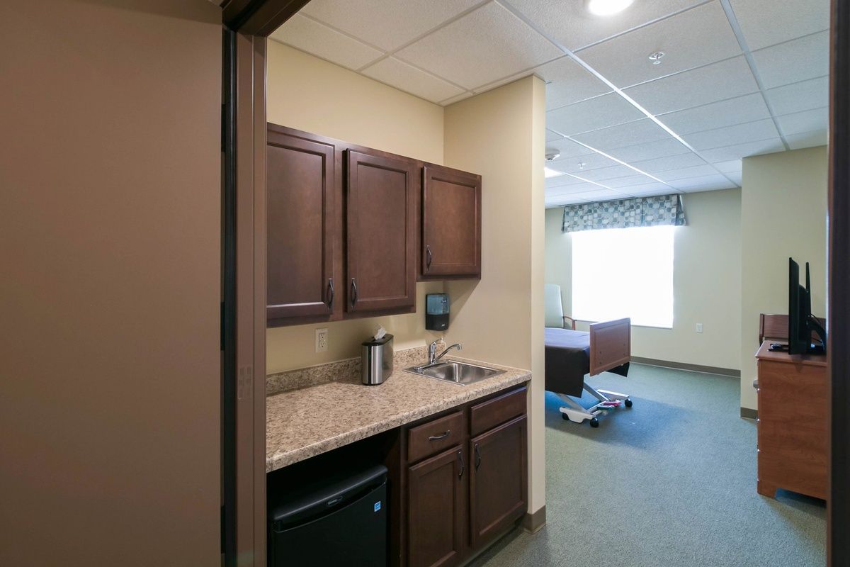 A compact kitchenette with wooden cabinets adjacent to a bedroom area.