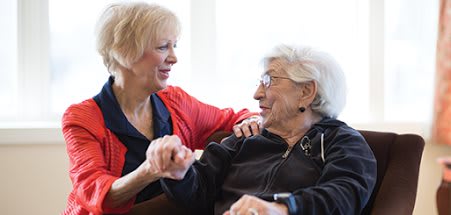A woman in a red sweater holding hands and conversing with an elderly woman.
