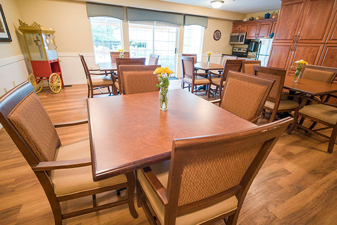 A modern dining area with wooden tables and chairs, featuring a kitchen in the background.