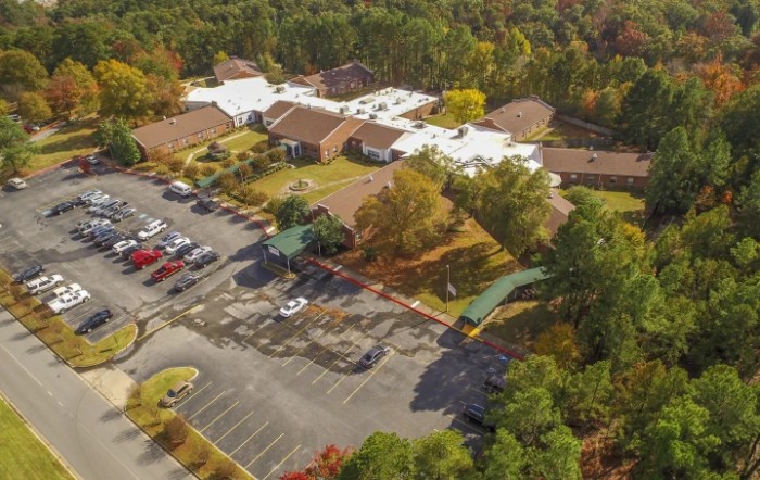 Aerial view of buildings surrounded by trees with a parking lot in the foreground.