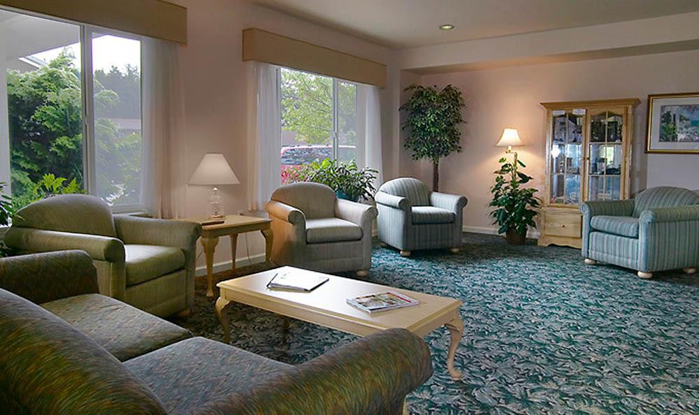 A cozy living room with comfortable sofas, armchairs, and a coffee table, featuring elegant lamps and lush indoor plants.