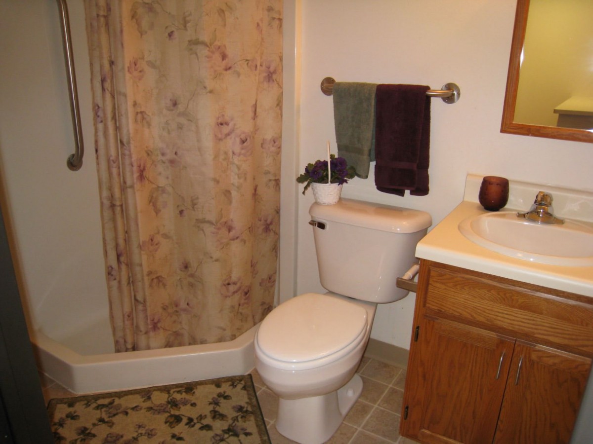 A cozy bathroom featuring a toilet, sink, and shower area with floral curtains.