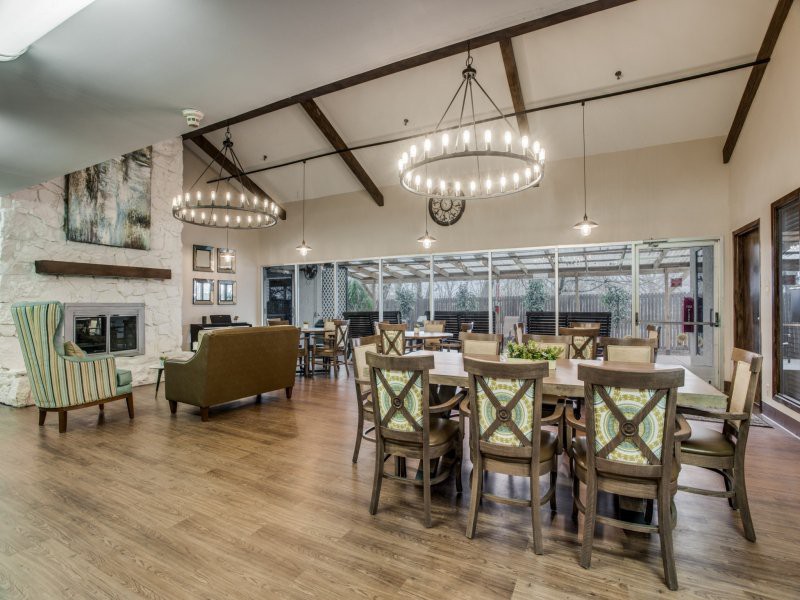 A spacious and elegantly designed dining and living area featuring large chandeliers, wooden flooring, and expansive windows.
