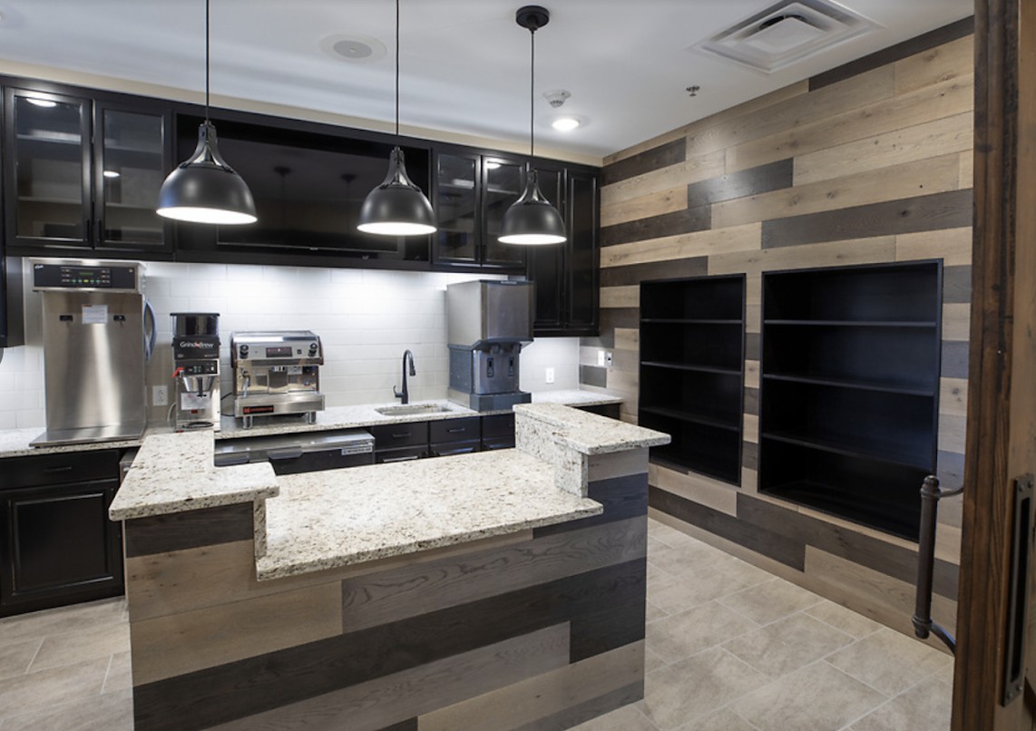 A modern kitchen area with sleek countertops, pendant lighting, and coffee-making equipment.