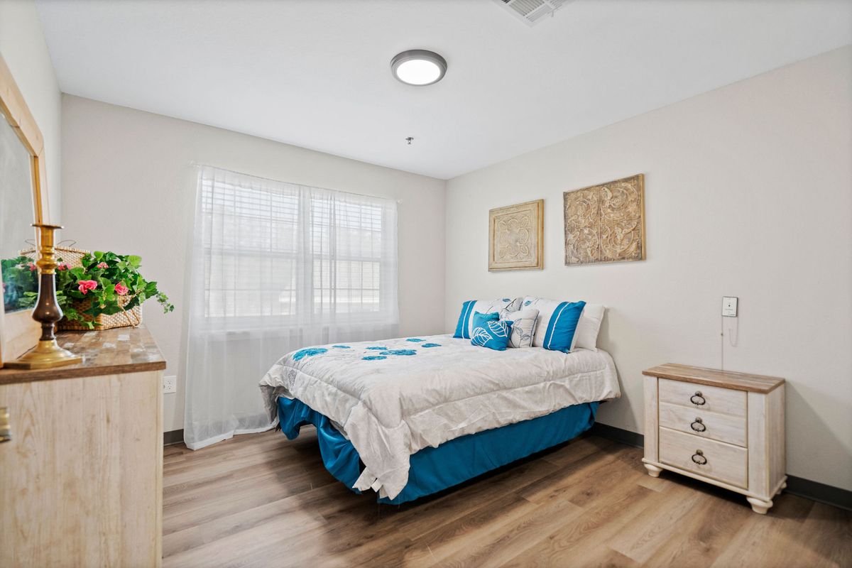 A cozy and minimalist bedroom with a neatly made bed, wooden flooring, and bright natural light coming through the window.