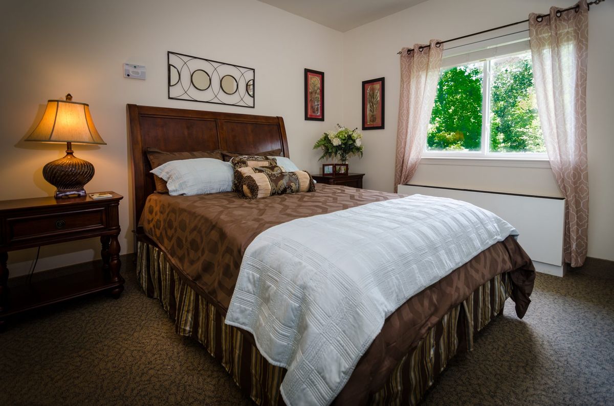 A cozy bedroom with a neatly made bed, decorative artwork, and a bright window letting in natural light.