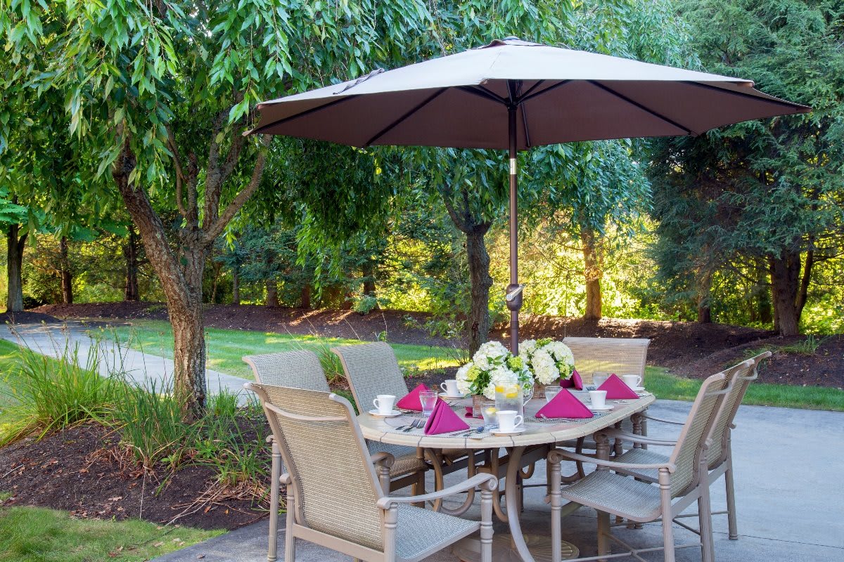 A beautifully set patio table under an umbrella in a lush garden setting.