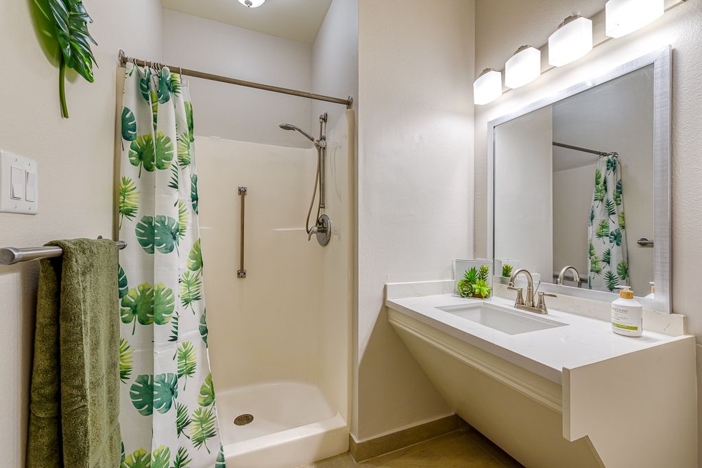 A modern bathroom featuring a shower with a tropical-patterned curtain, a sink with a large mirror, and bright lighting.