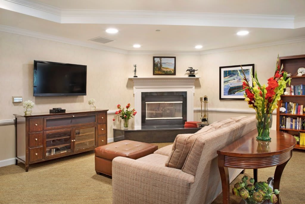 A cozy living room featuring a sofa, fireplace, and television, decorated with flowers and artwork.