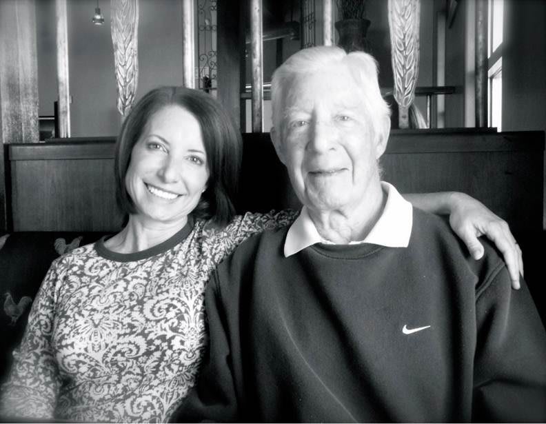 A black and white photo of two people smiling and sitting closely together indoors.
