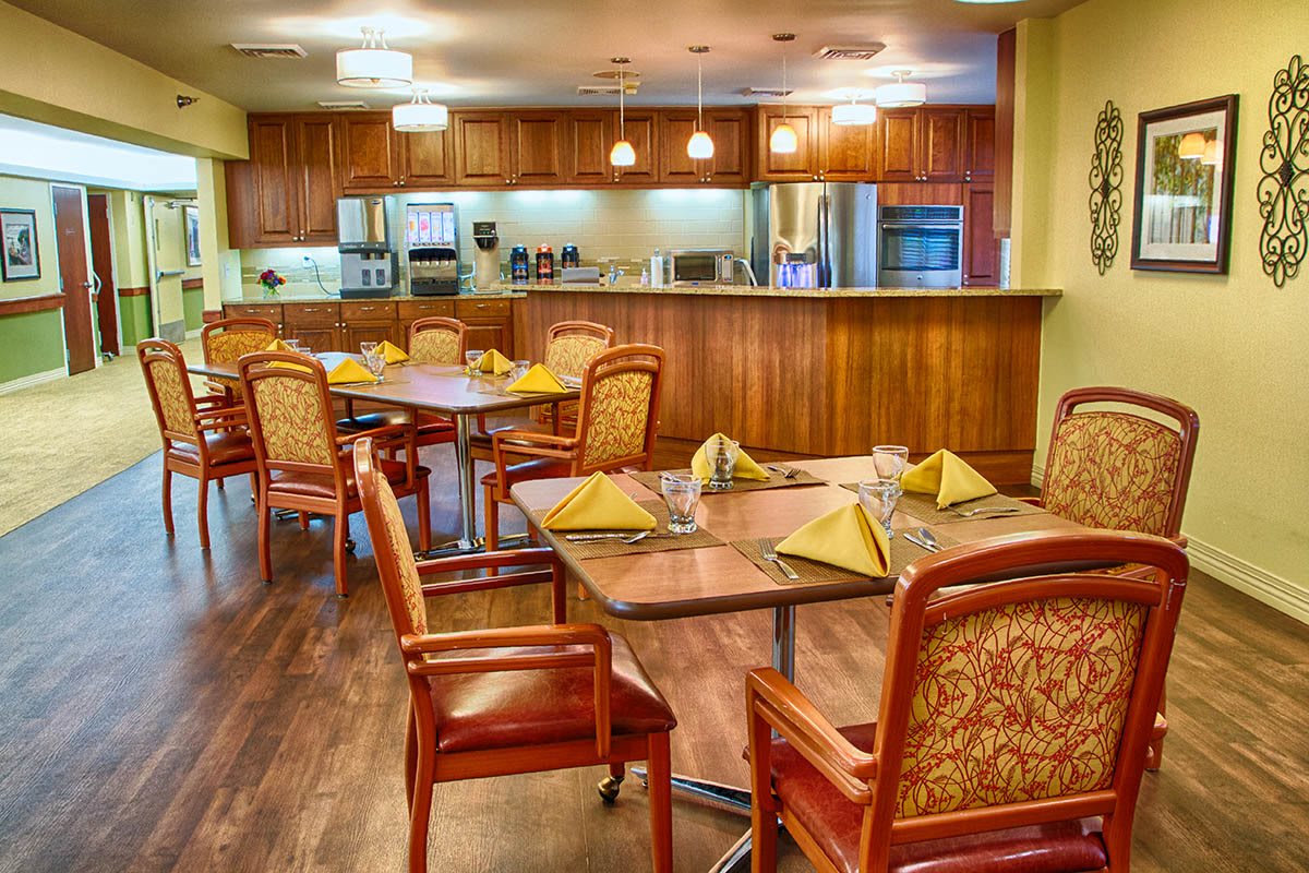 A cozy dining area with neatly arranged tables and chairs, adjacent to a modern kitchen.