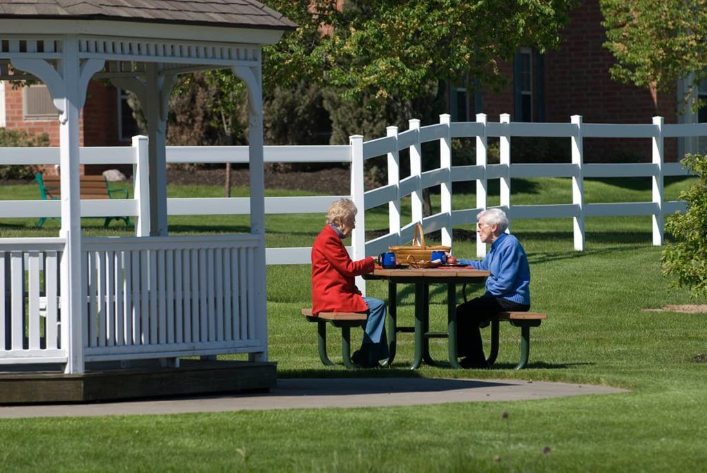 Two seniors enjoying a leisurely game at a picnic table in the park near a gazebo.