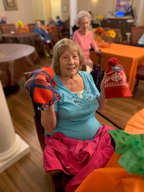 A smiling senior woman holds colorful gifts indoors.