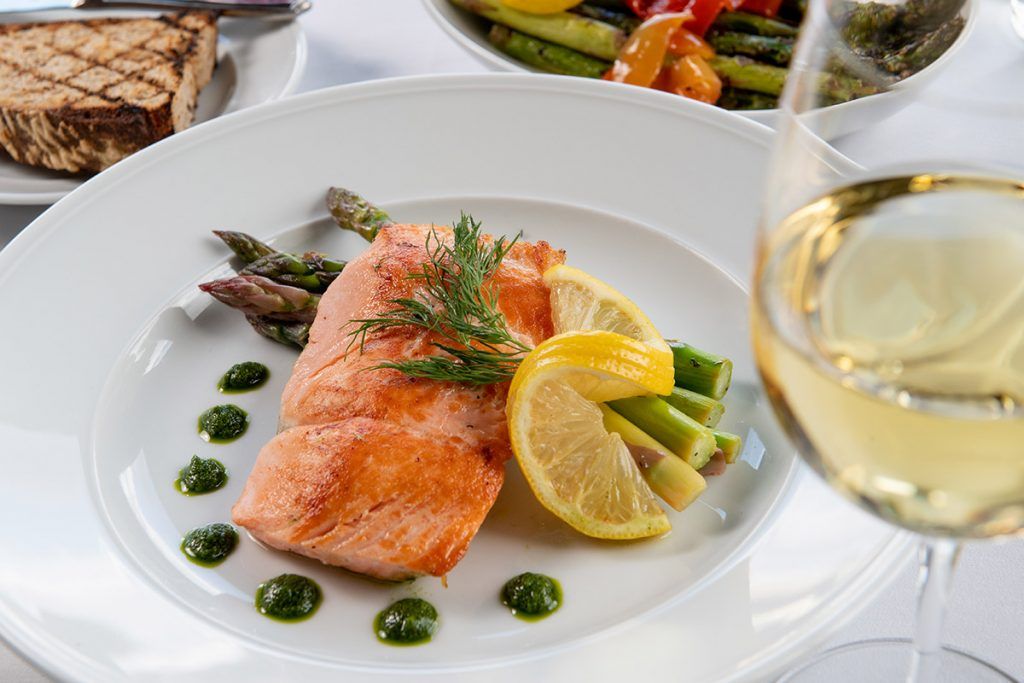 A gourmet dish featuring seared salmon served with asparagus, lemon slices, and a dill garnish.