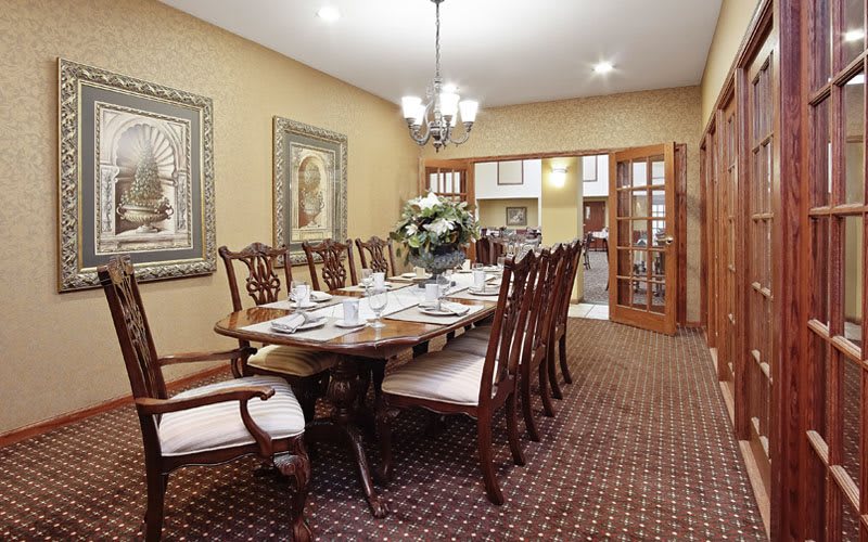 A spacious dining room with an elegant wooden table set for a meal, surrounded by matching chairs and adorned with a central chandelier.