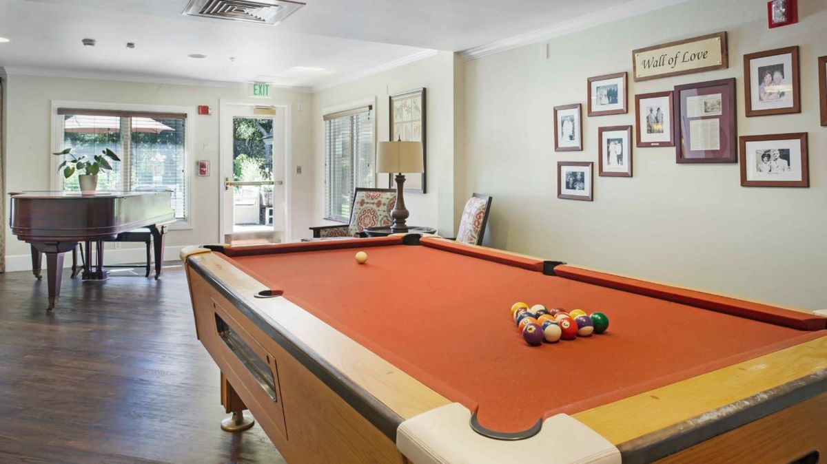 A cozy game room featuring a billiard table with an orange felt surface, surrounded by framed pictures on the wall.