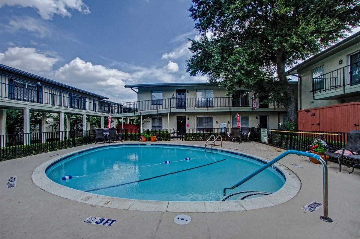 An outdoor swimming pool in the courtyard of a residential apartment complex under a clear blue sky.