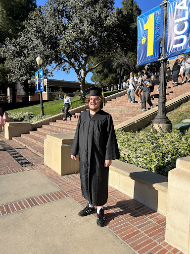A graduate proudly stands in their cap and gown on a university campus, celebrating their achievement.