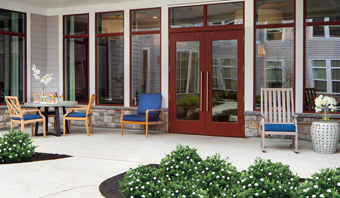 A cozy patio area with chairs and greenery outside a large glass door.