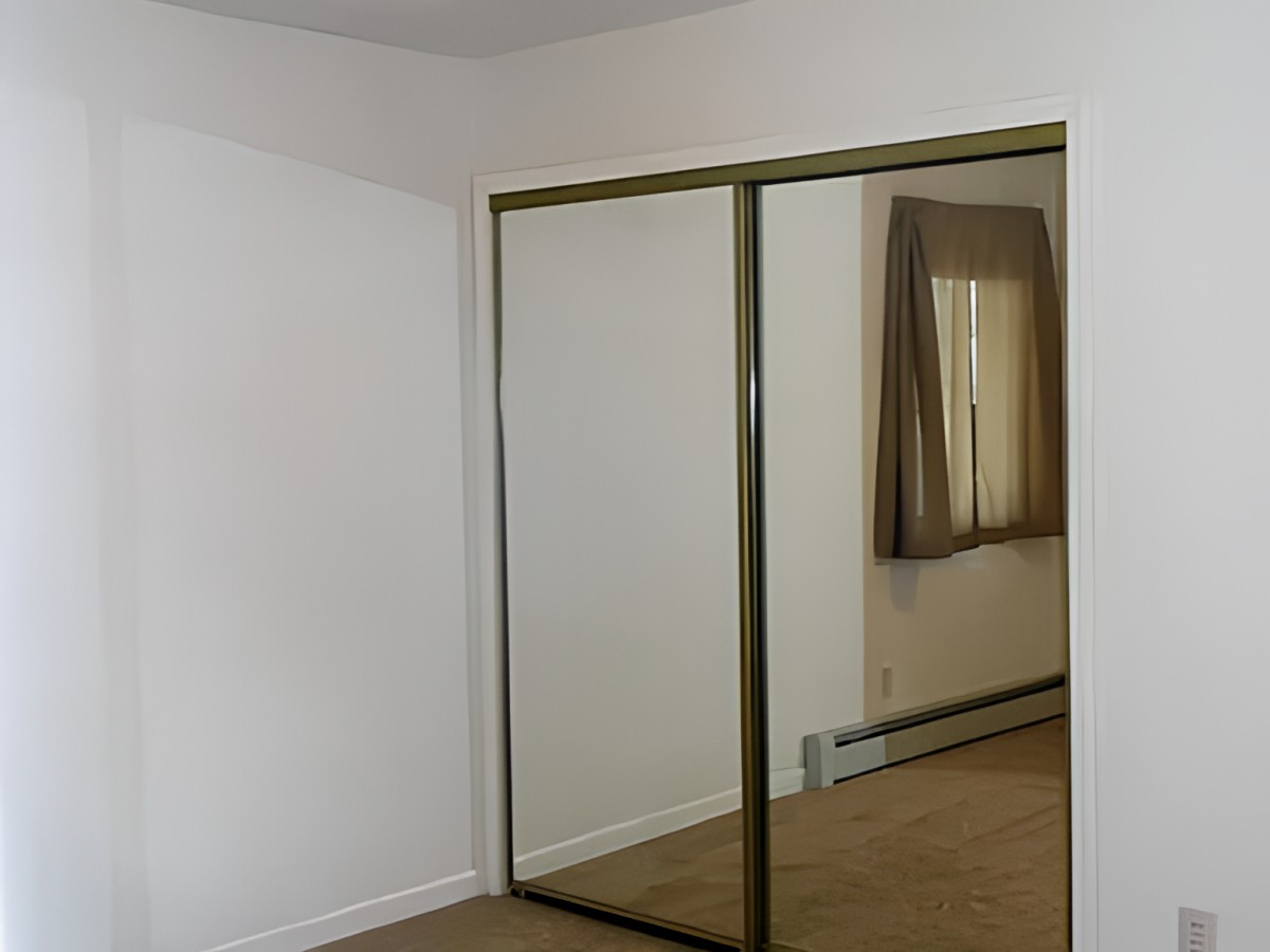 A simple empty room with mirrored closet doors and a window with curtains.