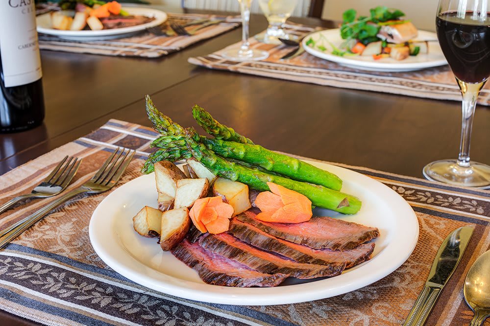 A delicious dinner plate featuring sliced steak, roasted potatoes, asparagus, and carrots.
