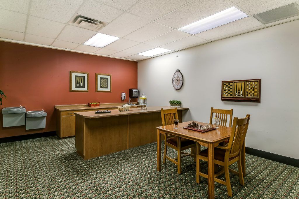 A tidy office with a desk, chairs, and computer setup, featuring a patterned carpet and decorative artwork on the walls.