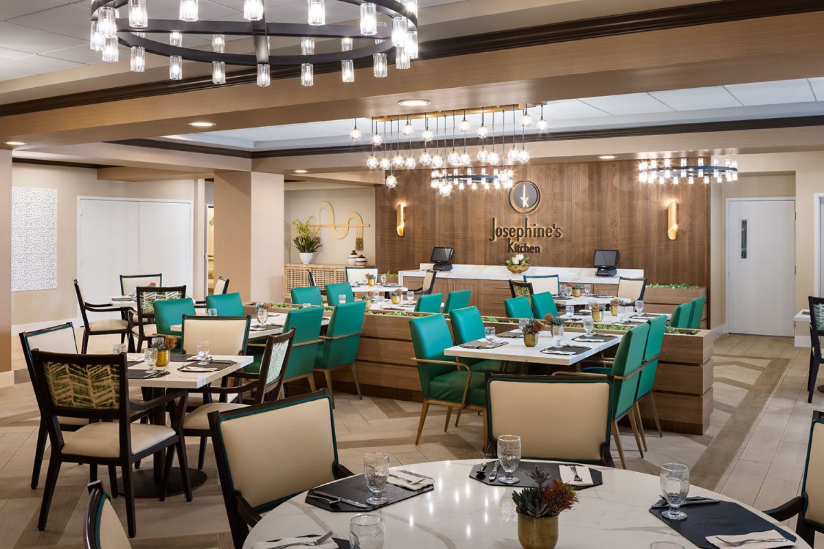 A modern restaurant interior featuring teal chairs, elegant chandeliers, and a warm wood-paneled design.