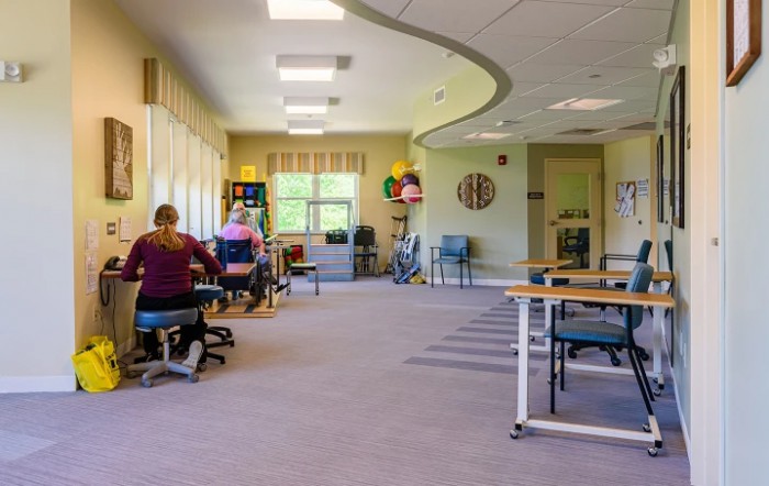A rehabilitation center therapy room with people exercising and various exercise equipment.