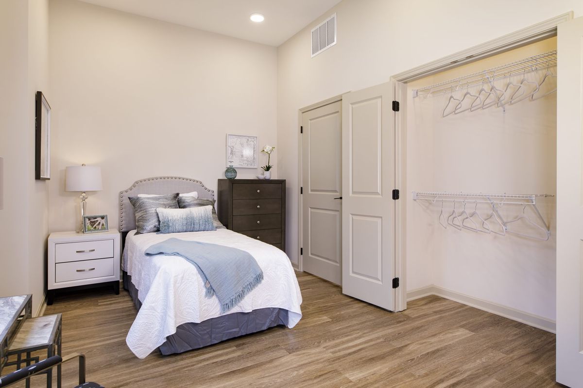 A minimalist bedroom with a single bed and neutral color scheme featuring wood flooring and a double-door closet.