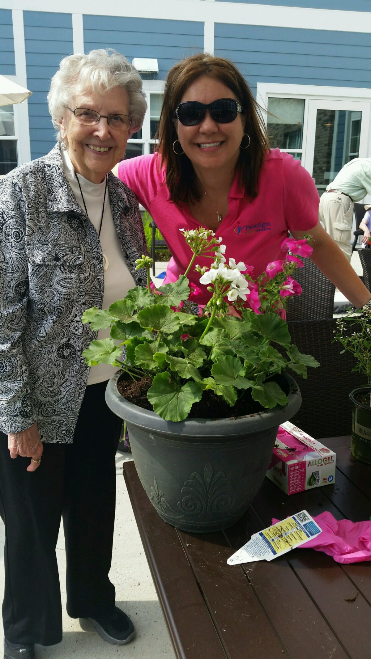 Two individuals smiling next to a potted flower arrangement.